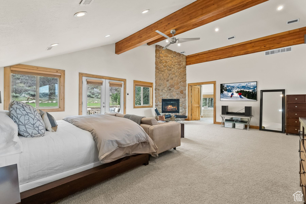 Carpeted bedroom with beamed ceiling, ceiling fan, multiple windows, and a stone fireplace