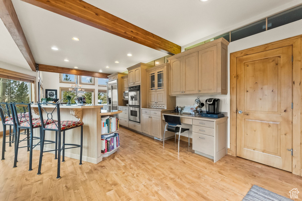 Kitchen featuring light hardwood / wood-style floors, a breakfast bar area, beam ceiling, stainless steel double oven, and kitchen peninsula