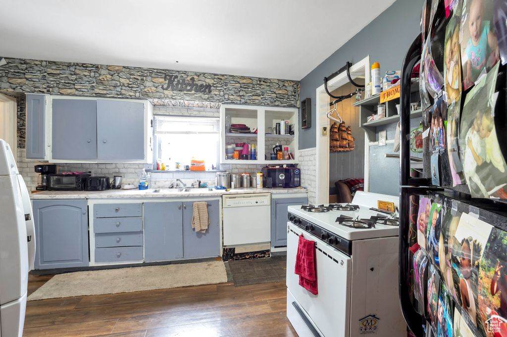Kitchen with sink, white appliances, tasteful backsplash, blue cabinetry, and dark hardwood / wood-style floors