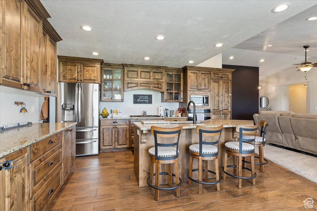 Kitchen featuring light stone countertops, dark hardwood / wood-style floors, a center island with sink, a breakfast bar area, and ceiling fan