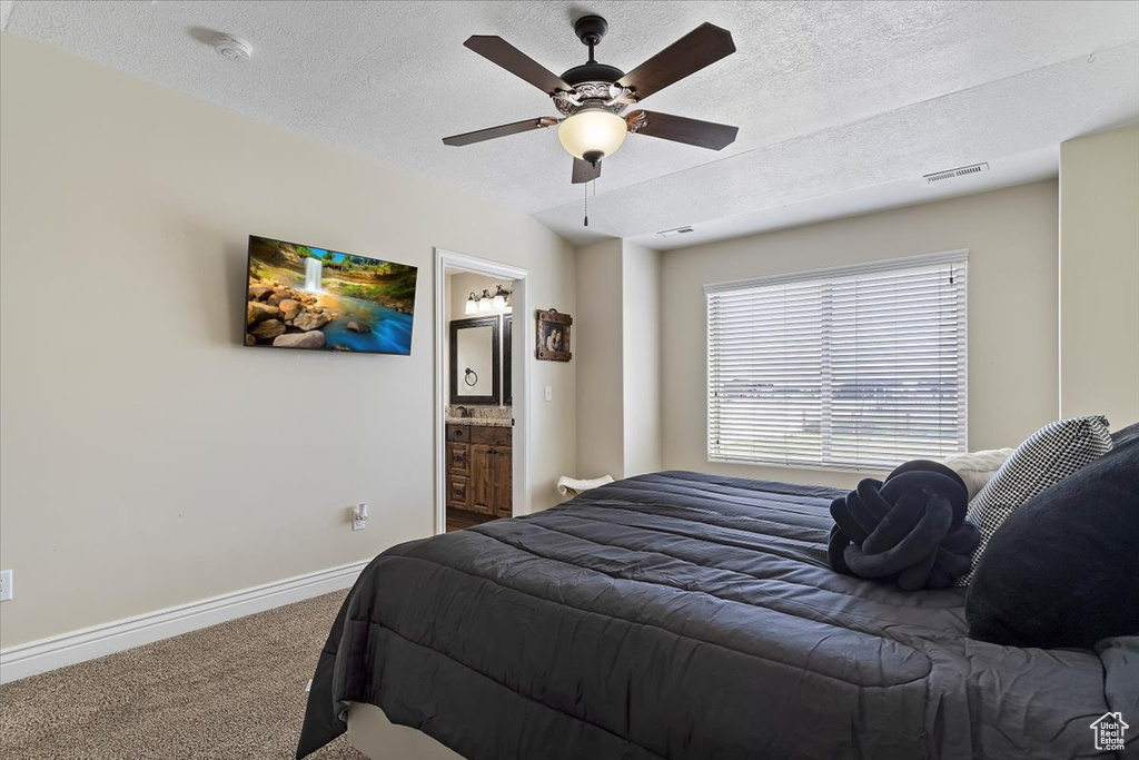 Carpeted bedroom with connected bathroom, ceiling fan, and a textured ceiling