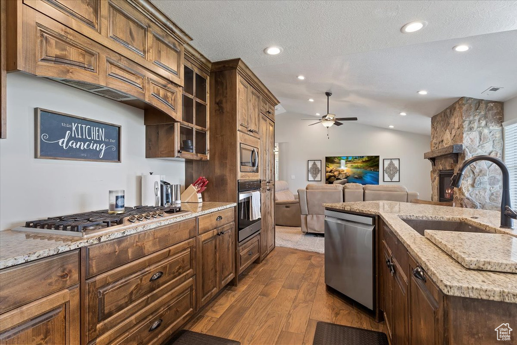 Kitchen with appliances with stainless steel finishes, ceiling fan, a stone fireplace, sink, and hardwood / wood-style flooring