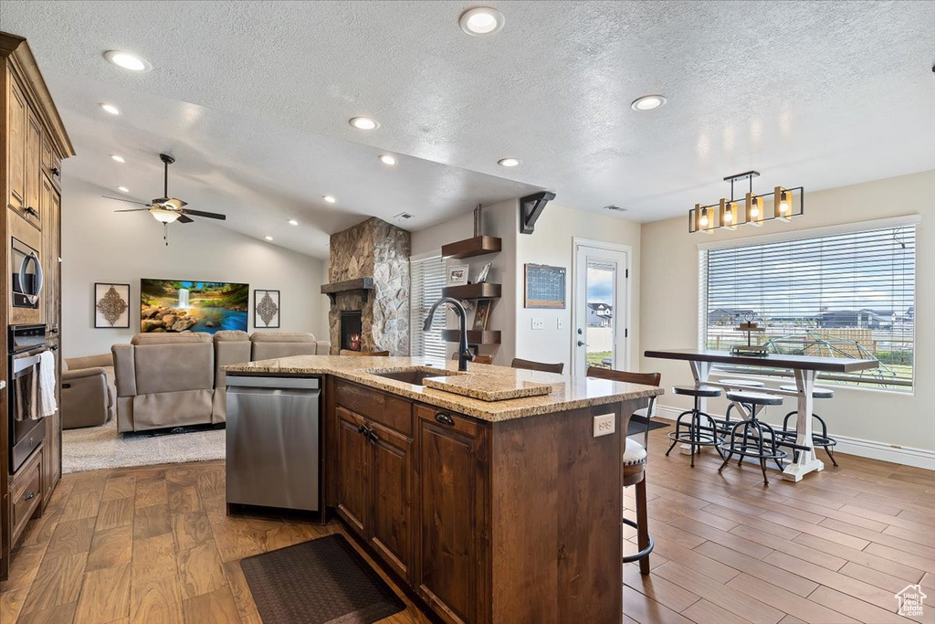 Kitchen featuring wood-type flooring, a kitchen island with sink, stainless steel appliances, sink, and lofted ceiling