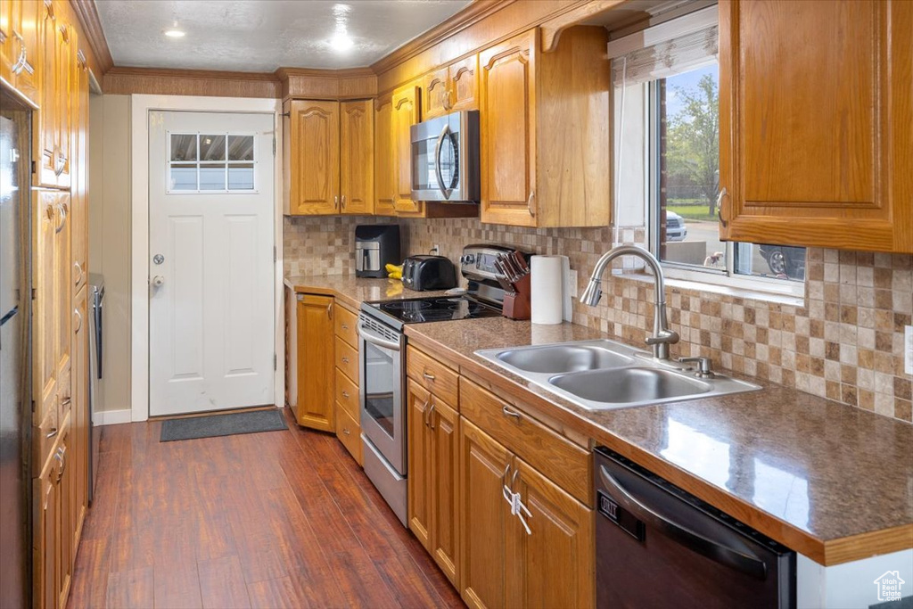 Kitchen featuring appliances with stainless steel finishes, sink, tasteful backsplash, dark hardwood / wood-style flooring, and crown molding
