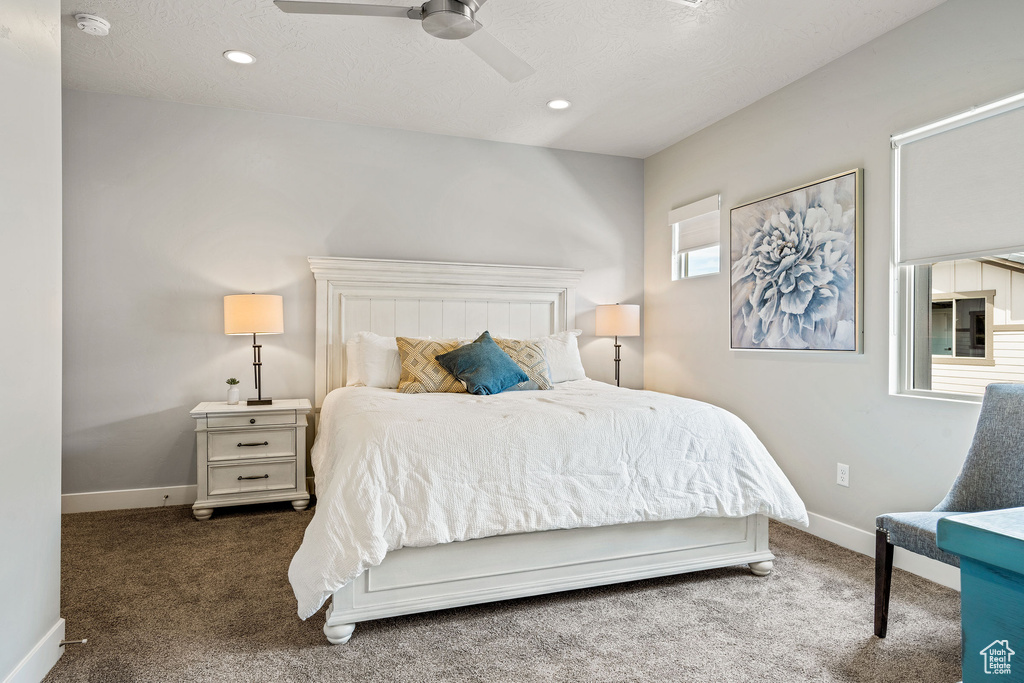 Bedroom with dark carpet, ceiling fan, and multiple windows