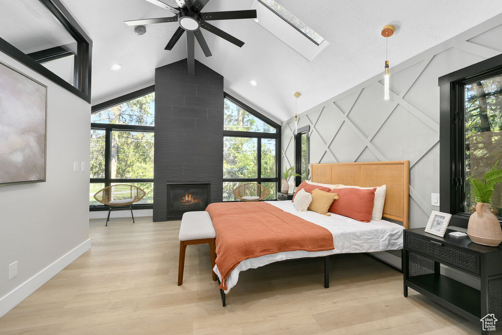 Bedroom with a skylight, light hardwood / wood-style flooring, high vaulted ceiling, and a fireplace