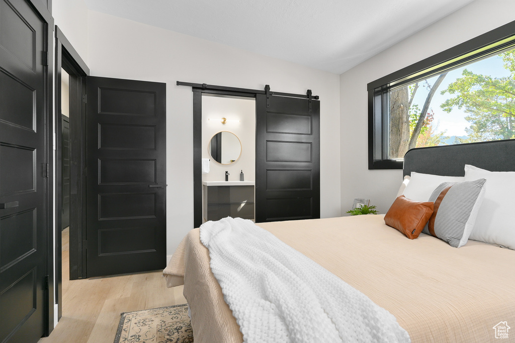 Bedroom featuring ensuite bath, light wood-type flooring, and a barn door