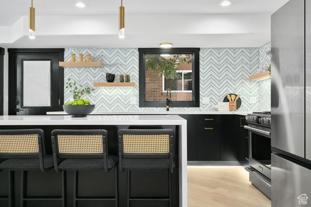 Bar with backsplash, light hardwood / wood-style flooring, appliances with stainless steel finishes, sink, and pendant lighting