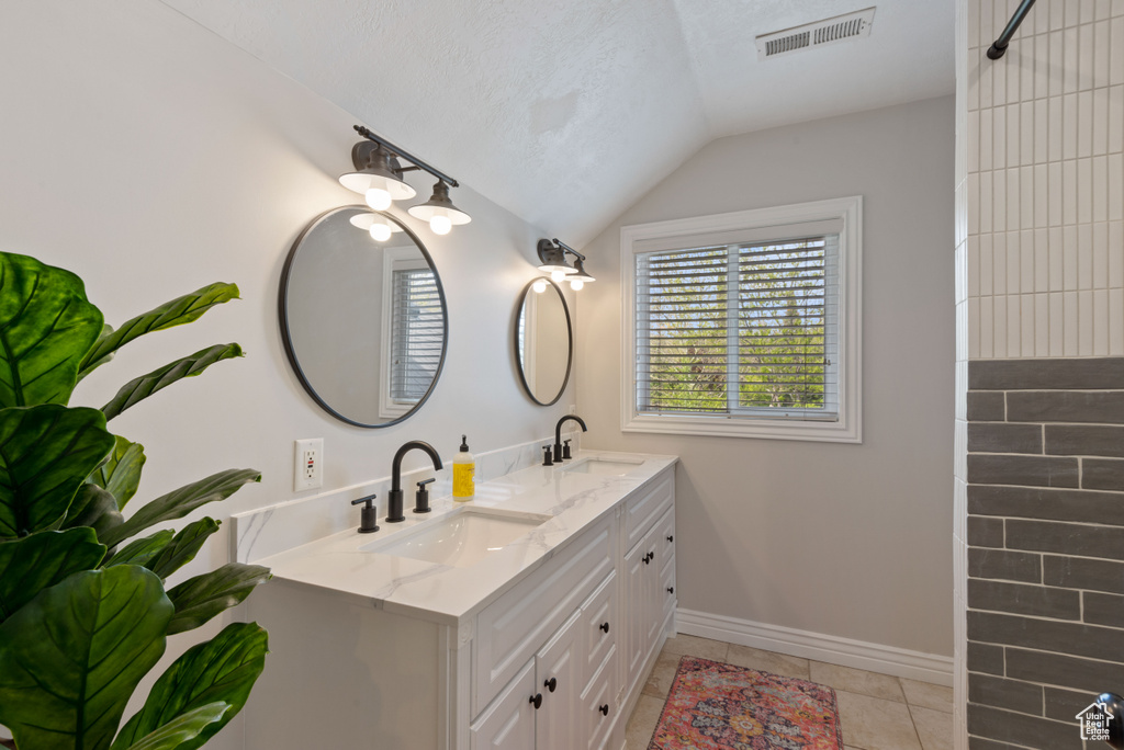 Bathroom featuring tile flooring, vaulted ceiling, double vanity, and a textured ceiling