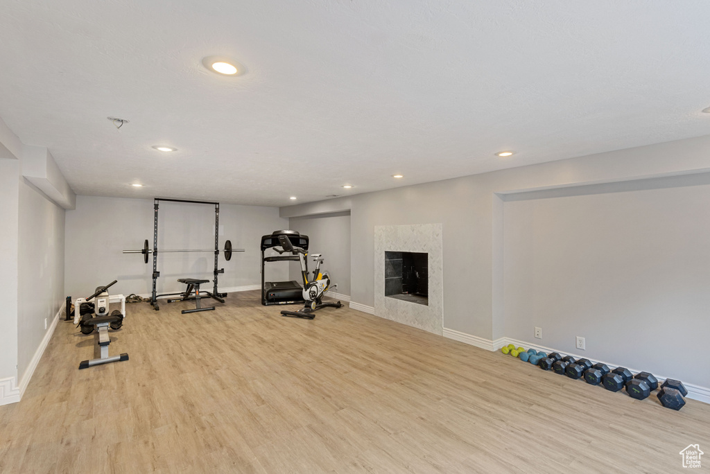 Exercise room with a premium fireplace and light wood-type flooring