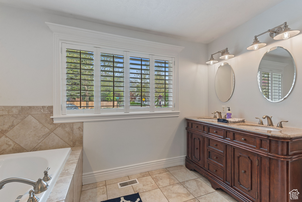 Bathroom with dual sinks, a relaxing tiled bath, a wealth of natural light, and vanity with extensive cabinet space