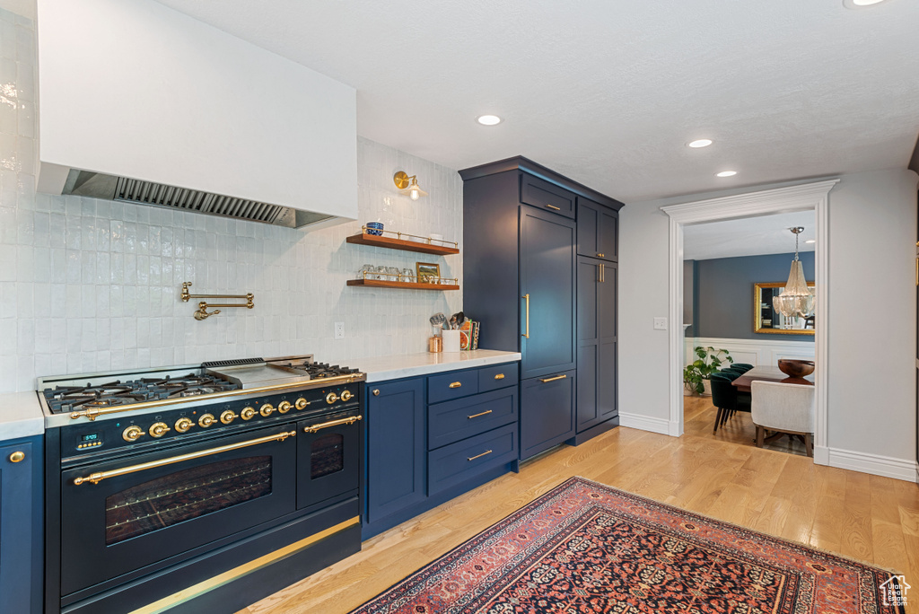 Kitchen with backsplash, blue cabinets, range with two ovens, and light wood-type flooring