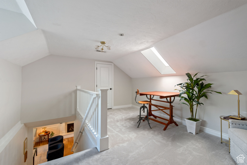 Home office featuring light colored carpet and vaulted ceiling with skylight