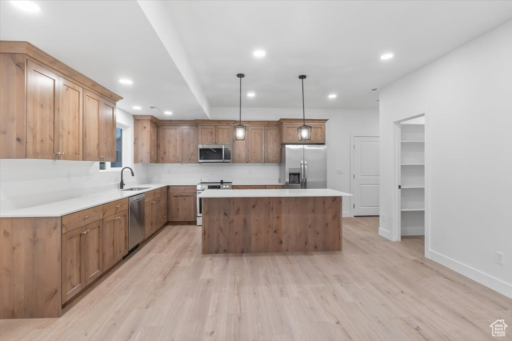 Kitchen featuring appliances with stainless steel finishes, a kitchen island, light wood-type flooring, and decorative light fixtures