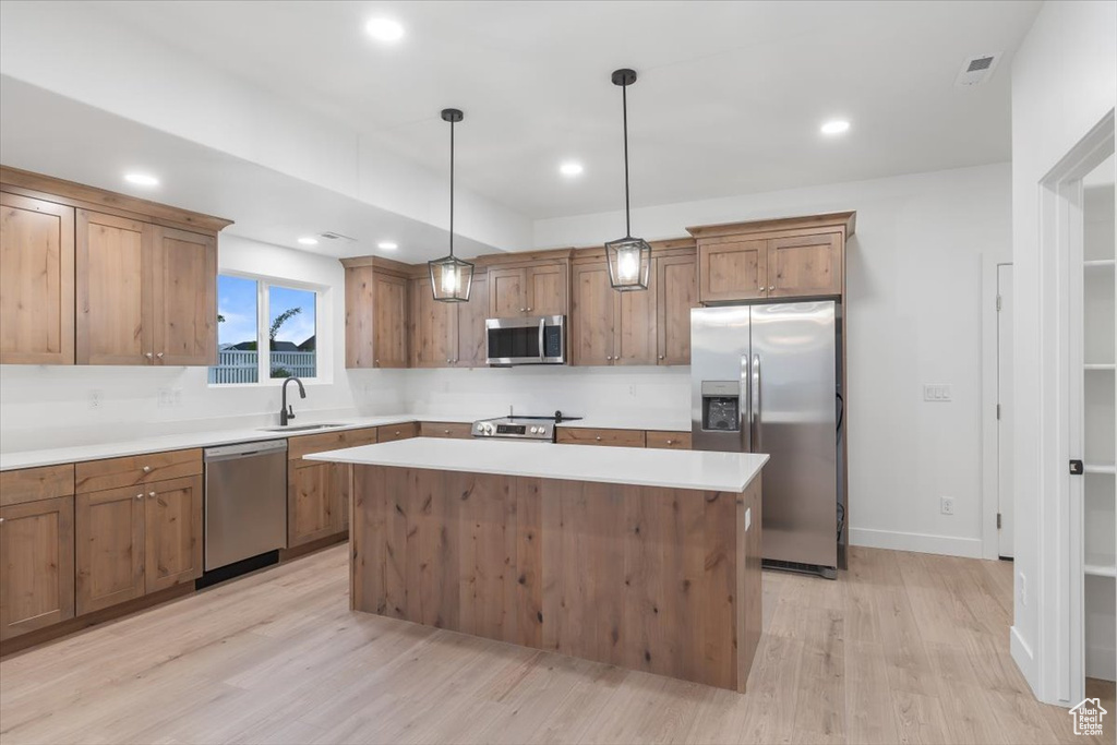 Kitchen featuring a kitchen island, sink, light hardwood / wood-style floors, stainless steel appliances, and pendant lighting