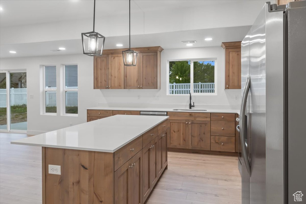 Kitchen featuring decorative light fixtures, stainless steel refrigerator, sink, a center island, and light wood-type flooring