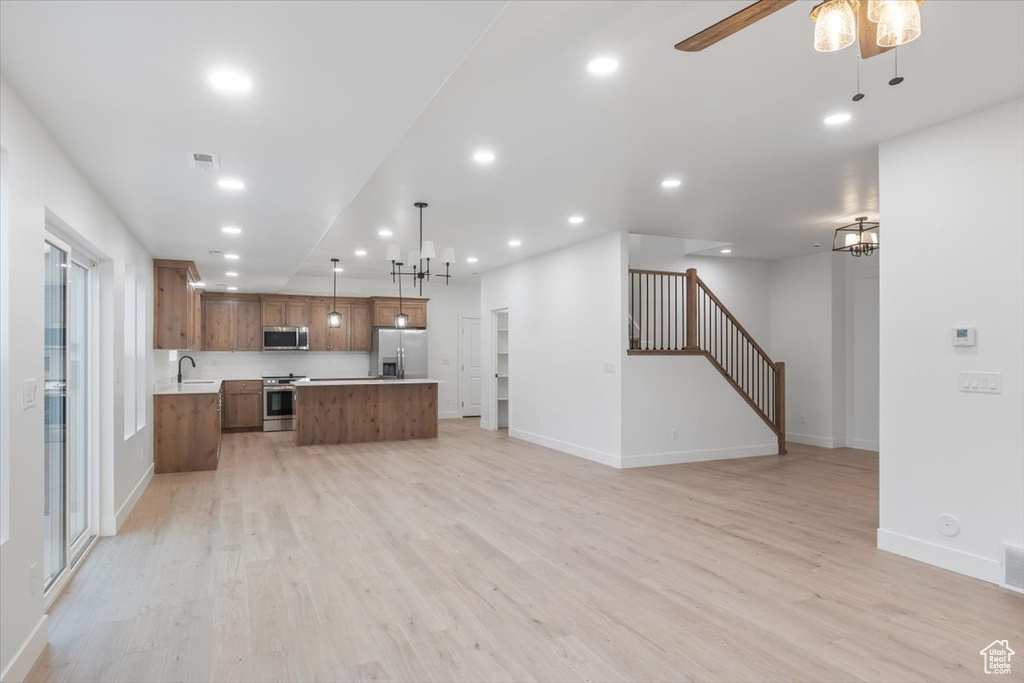 Kitchen with a center island, hanging light fixtures, light wood-type flooring, appliances with stainless steel finishes, and sink