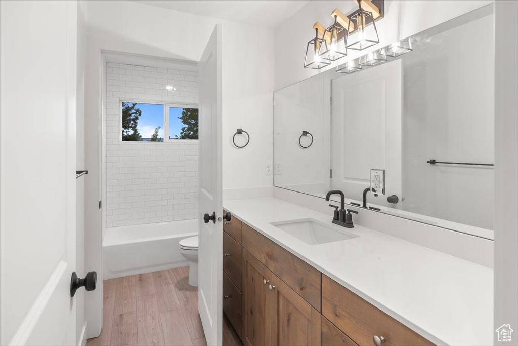 Full bathroom with tiled shower / bath combo, hardwood / wood-style floors, vanity, and toilet