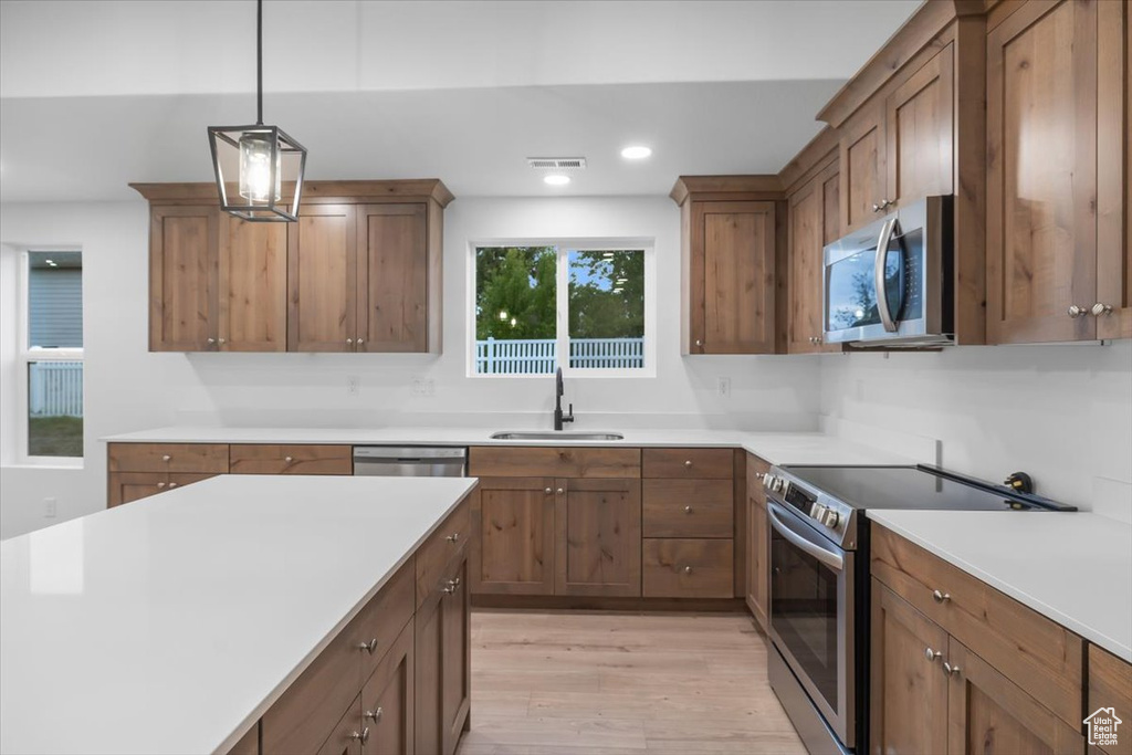 Kitchen with pendant lighting, backsplash, appliances with stainless steel finishes, sink, and light hardwood / wood-style floors