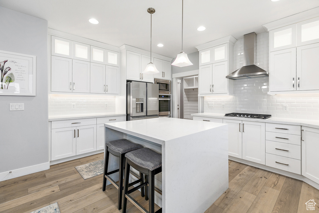 Kitchen featuring light hardwood / wood-style flooring, stainless steel appliances, tasteful backsplash, wall chimney exhaust hood, and white cabinetry