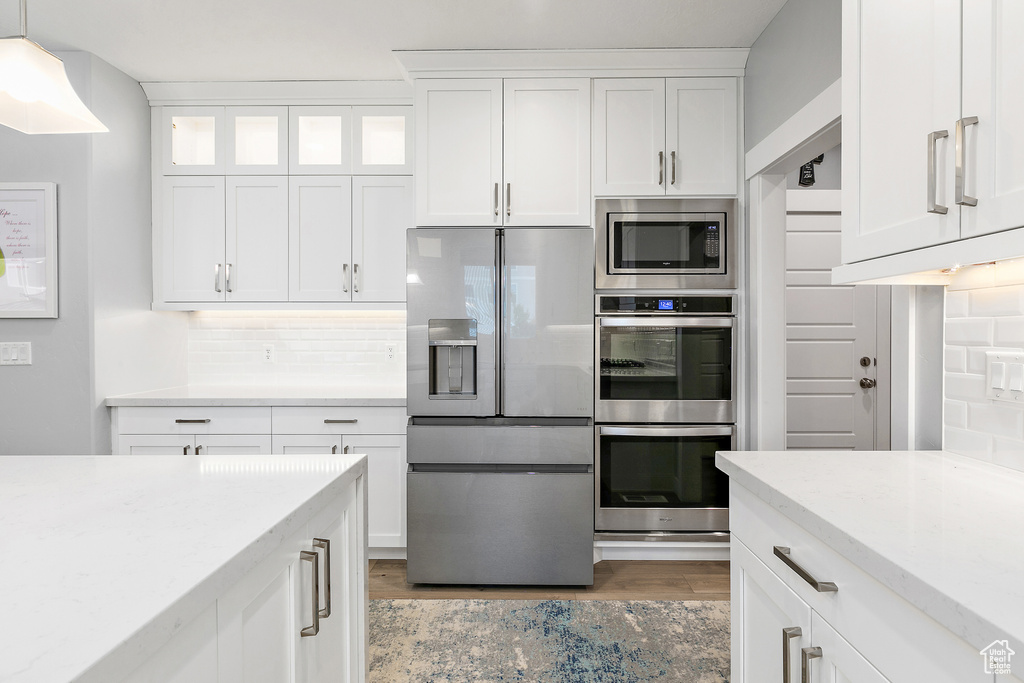 Kitchen with appliances with stainless steel finishes, white cabinets, light hardwood / wood-style floors, backsplash, and hanging light fixtures