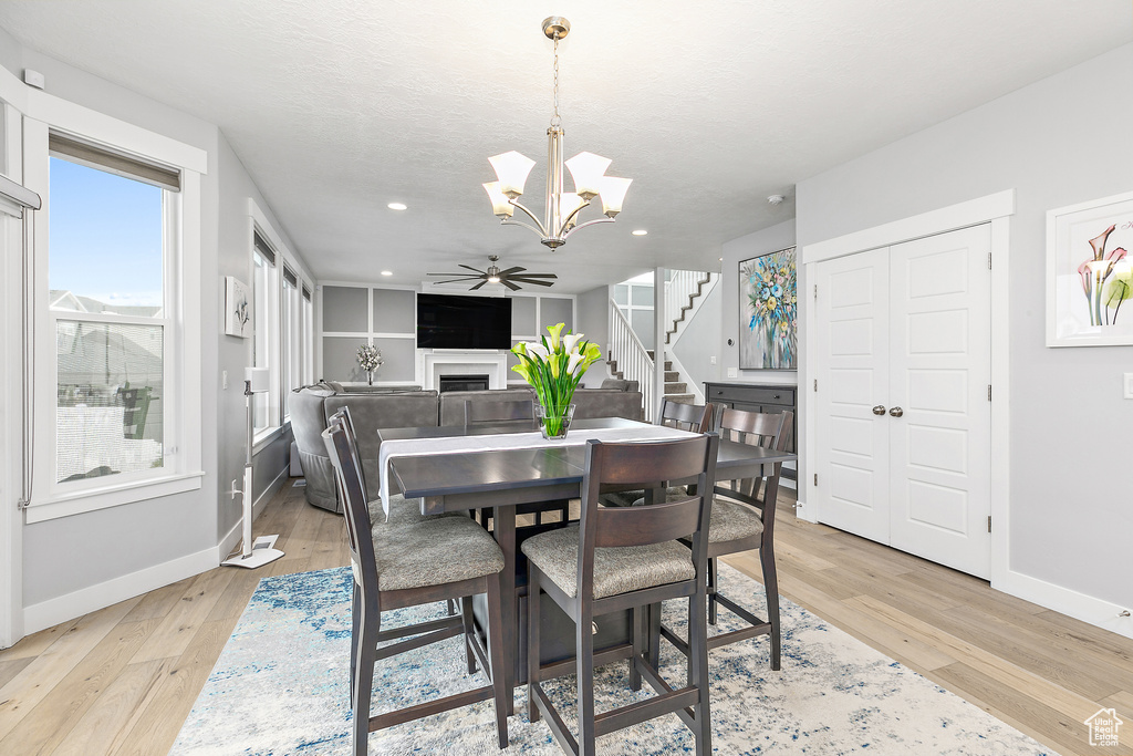 Dining room with ceiling fan with notable chandelier and light hardwood / wood-style flooring