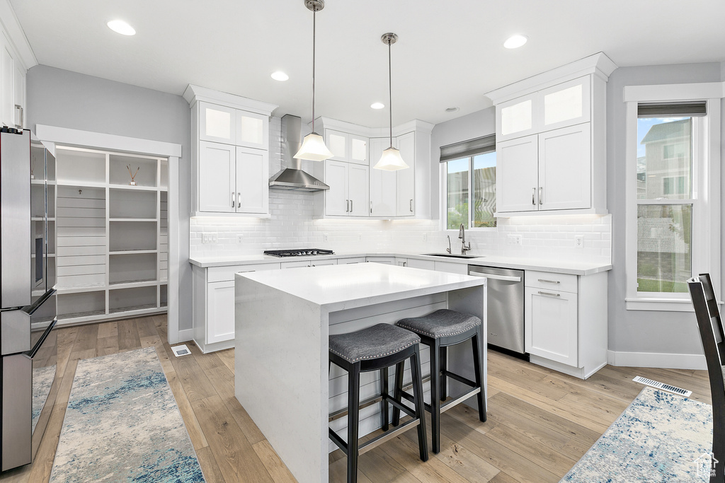 Kitchen with white cabinets, appliances with stainless steel finishes, wall chimney range hood, and light wood-type flooring