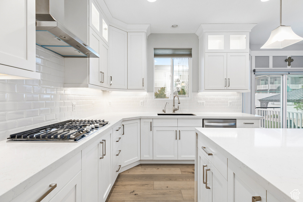 Kitchen featuring tasteful backsplash, light hardwood / wood-style floors, wall chimney range hood, and white cabinetry