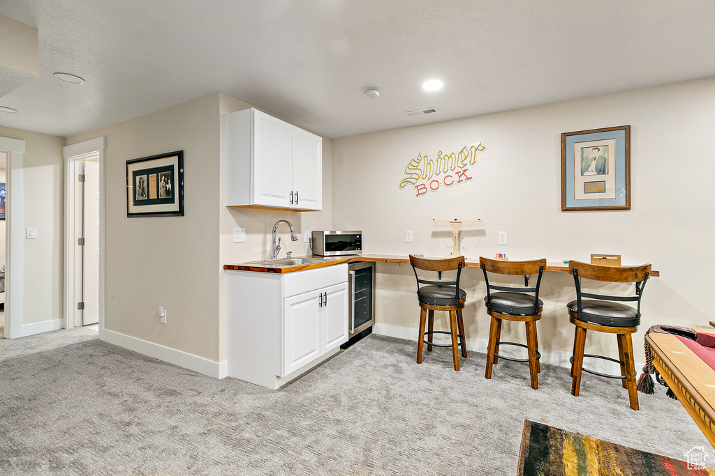 Kitchen with light carpet, white cabinetry, sink, and beverage cooler