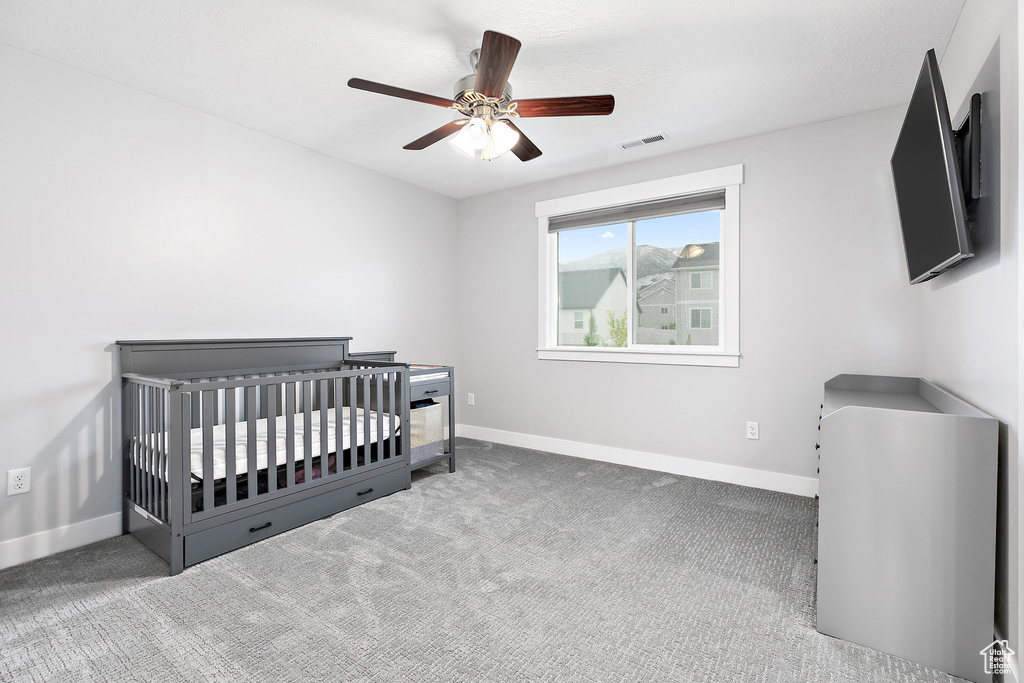 Bedroom featuring dark colored carpet, a nursery area, and ceiling fan