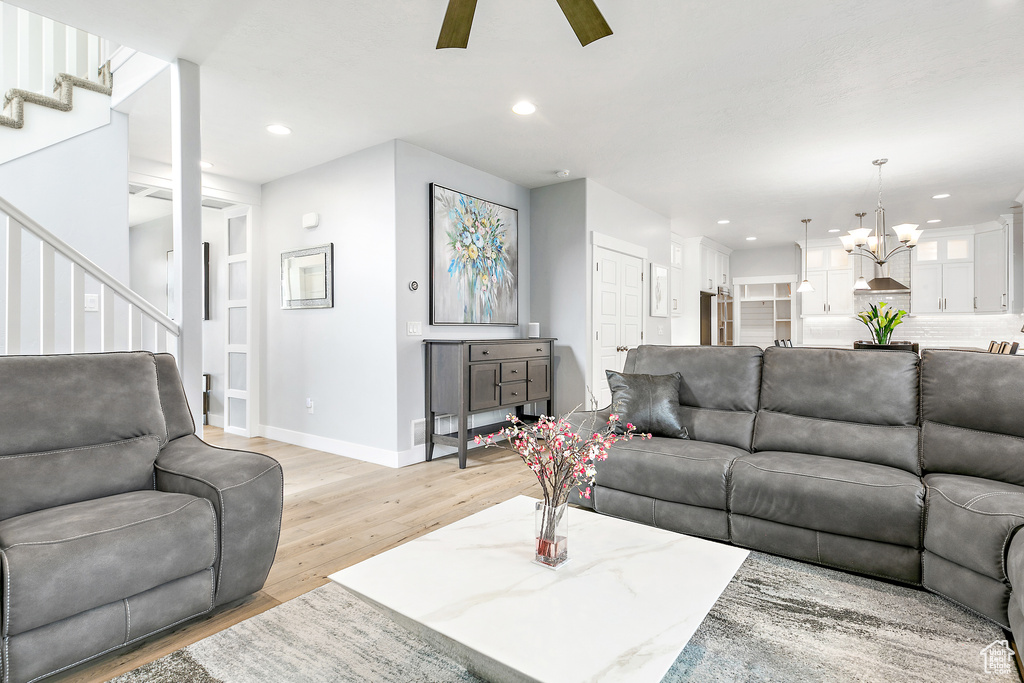 Living room with ceiling fan with notable chandelier and light wood-type flooring