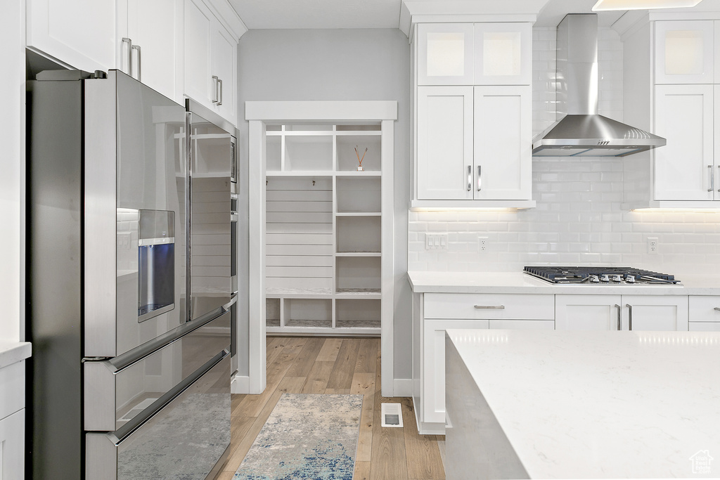 Kitchen featuring white cabinets, light hardwood / wood-style flooring, wall chimney exhaust hood, and stainless steel appliances