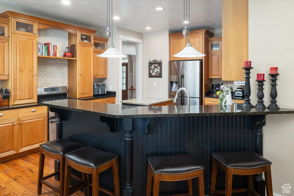 Kitchen featuring hanging light fixtures, dark stone countertops, light wood-type flooring, and stainless steel appliances