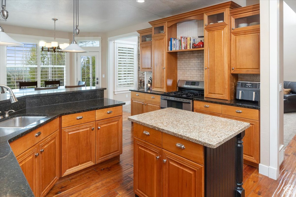Kitchen with backsplash, stainless steel range with gas stovetop, wood-type flooring, dark stone countertops, and sink