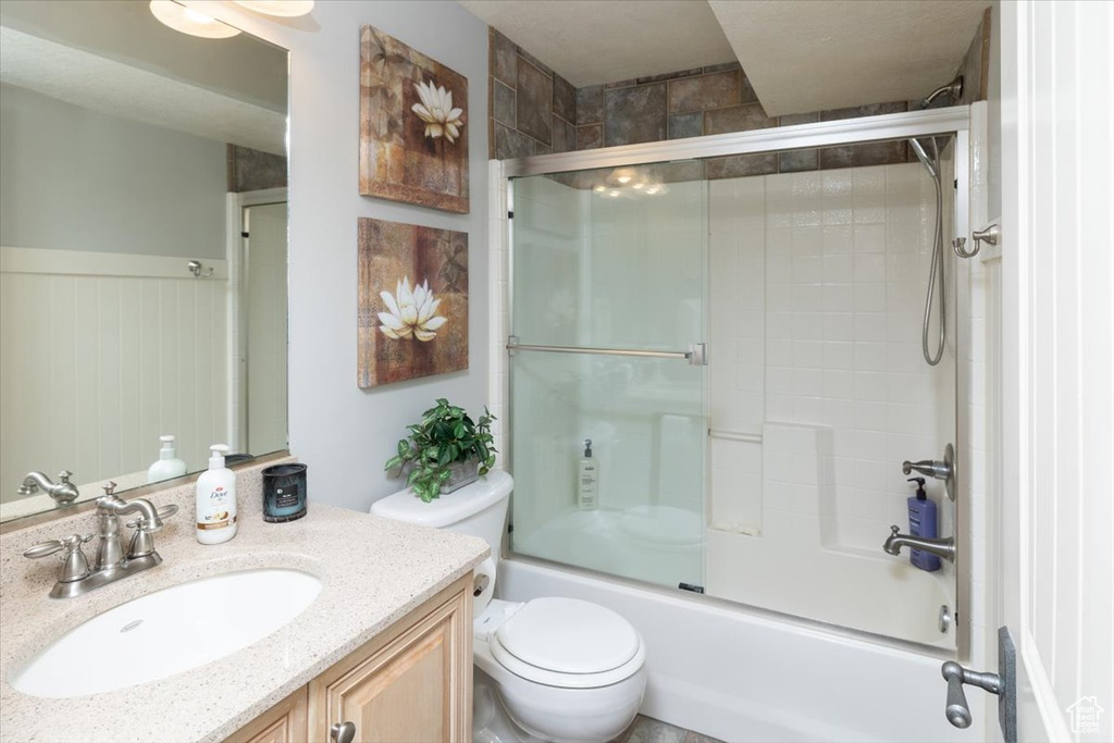 Full bathroom featuring toilet, bath / shower combo with glass door, and vanity