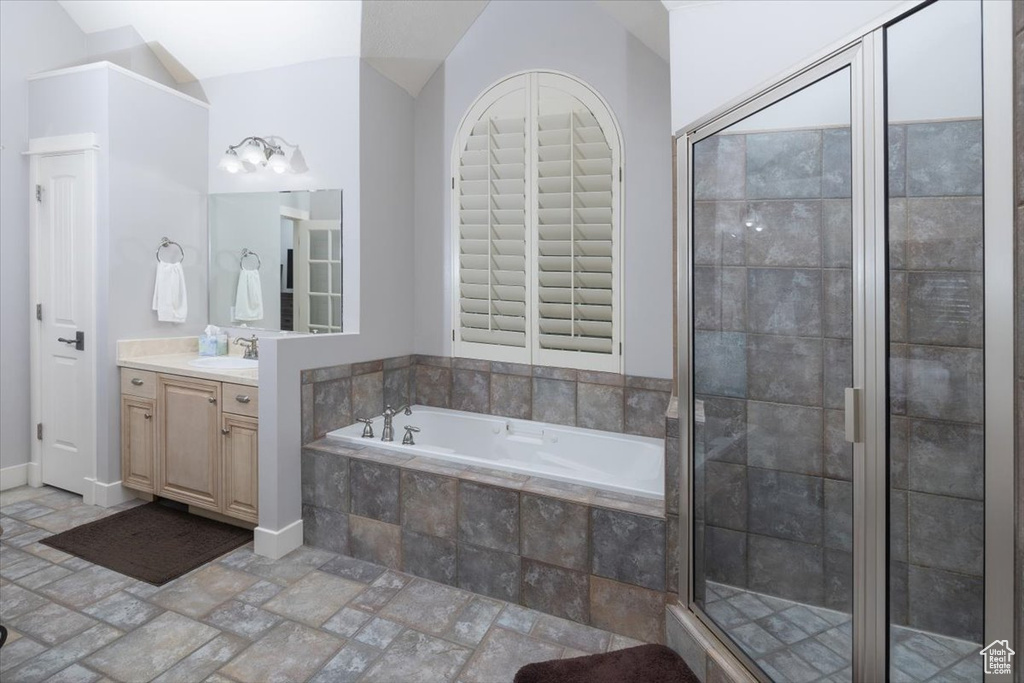 Bathroom featuring tile flooring, shower with separate bathtub, vanity, and lofted ceiling