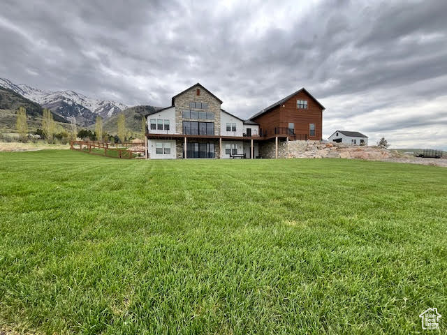 Back of house with a yard, a mountain view, and stone siding