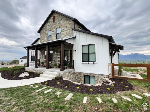 Modern inspired farmhouse featuring board and batten siding, a mountain view, covered porch, and stone siding