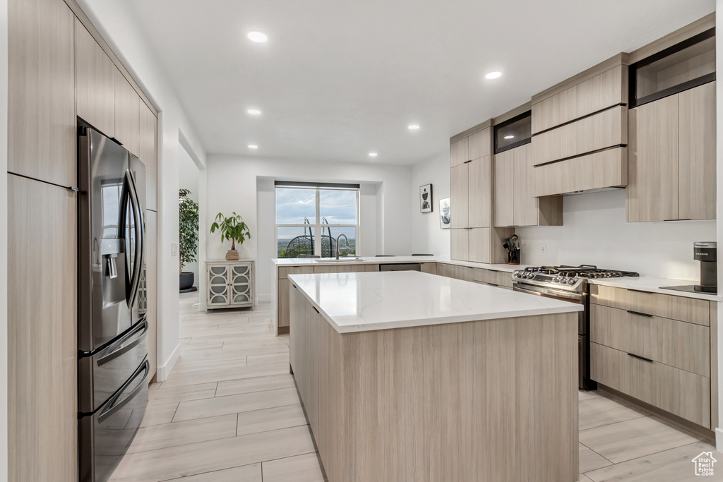 Kitchen featuring a center island, sink, gas range oven, stainless steel fridge with ice dispenser, and light stone countertops