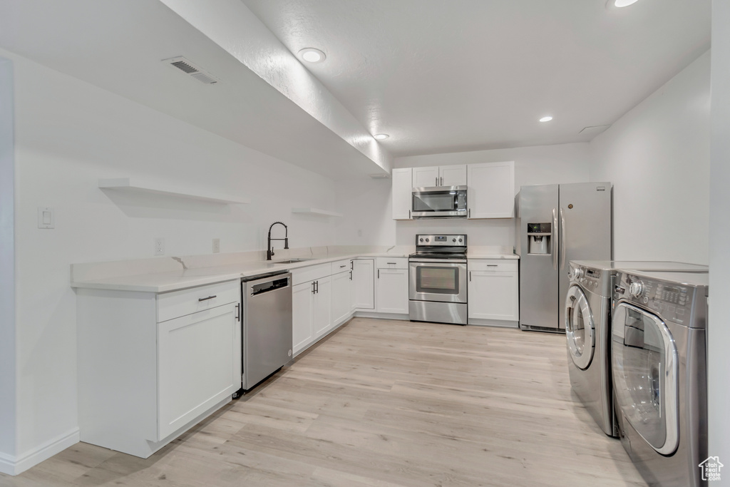 Kitchen with light wood-type flooring, washer and clothes dryer, kitchen peninsula, appliances with stainless steel finishes, and white cabinets