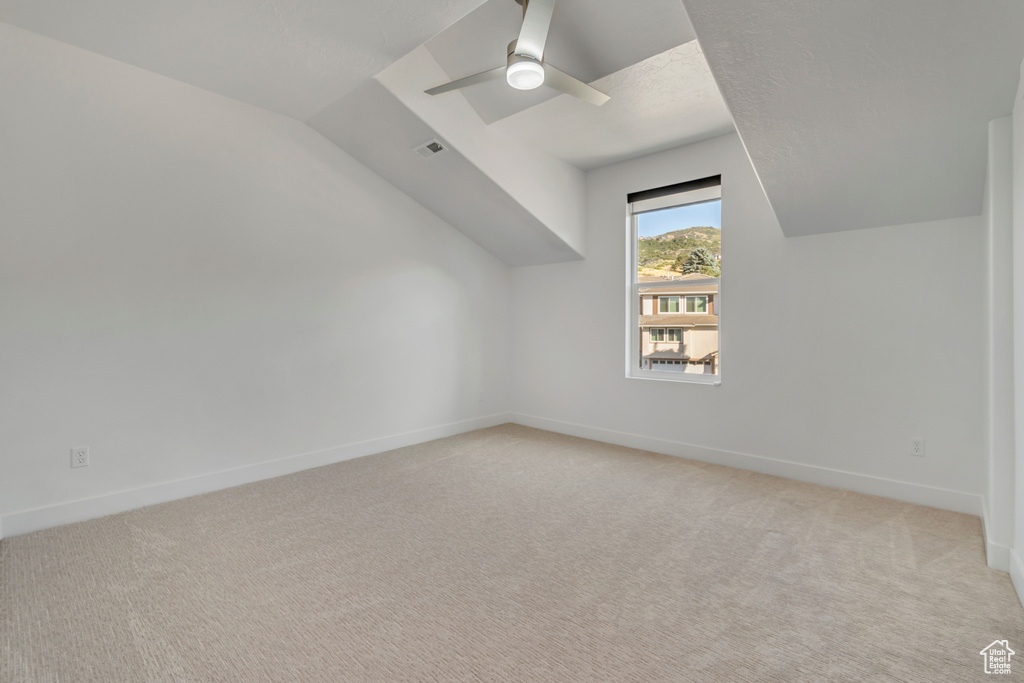 Additional living space featuring light colored carpet, ceiling fan, and vaulted ceiling