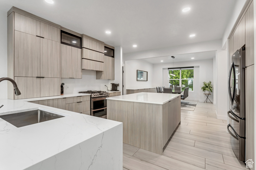 Kitchen with a center island, hanging light fixtures, light stone countertops, appliances with stainless steel finishes, and sink