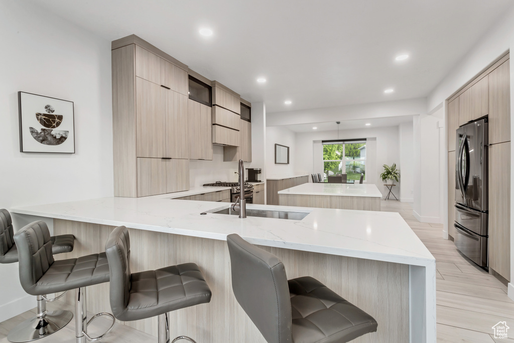 Kitchen featuring light stone countertops, kitchen peninsula, stainless steel refrigerator, a kitchen breakfast bar, and light wood-type flooring