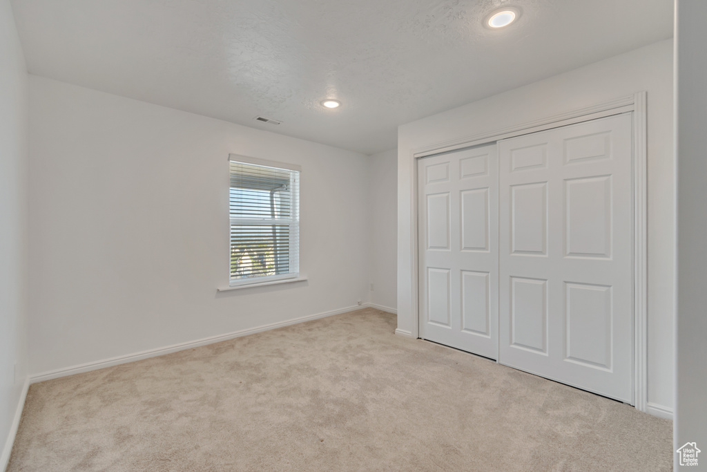 Unfurnished bedroom featuring light carpet, a textured ceiling, and a closet