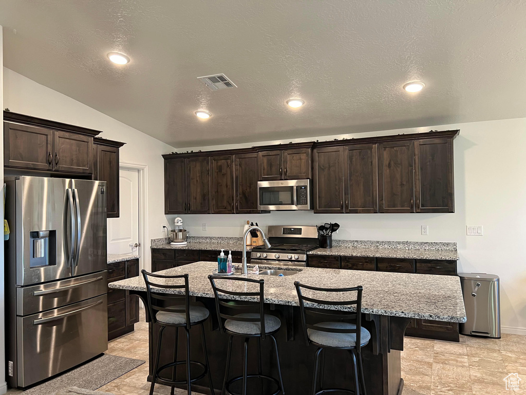 Kitchen featuring appliances with stainless steel finishes, a breakfast bar area, a center island with sink, and light tile floors