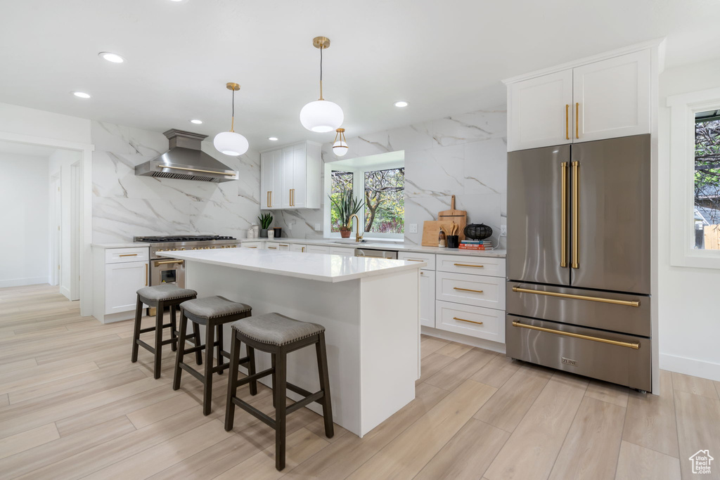Kitchen featuring pendant lighting, white cabinets, appliances with stainless steel finishes, wall chimney range hood, and tasteful backsplash