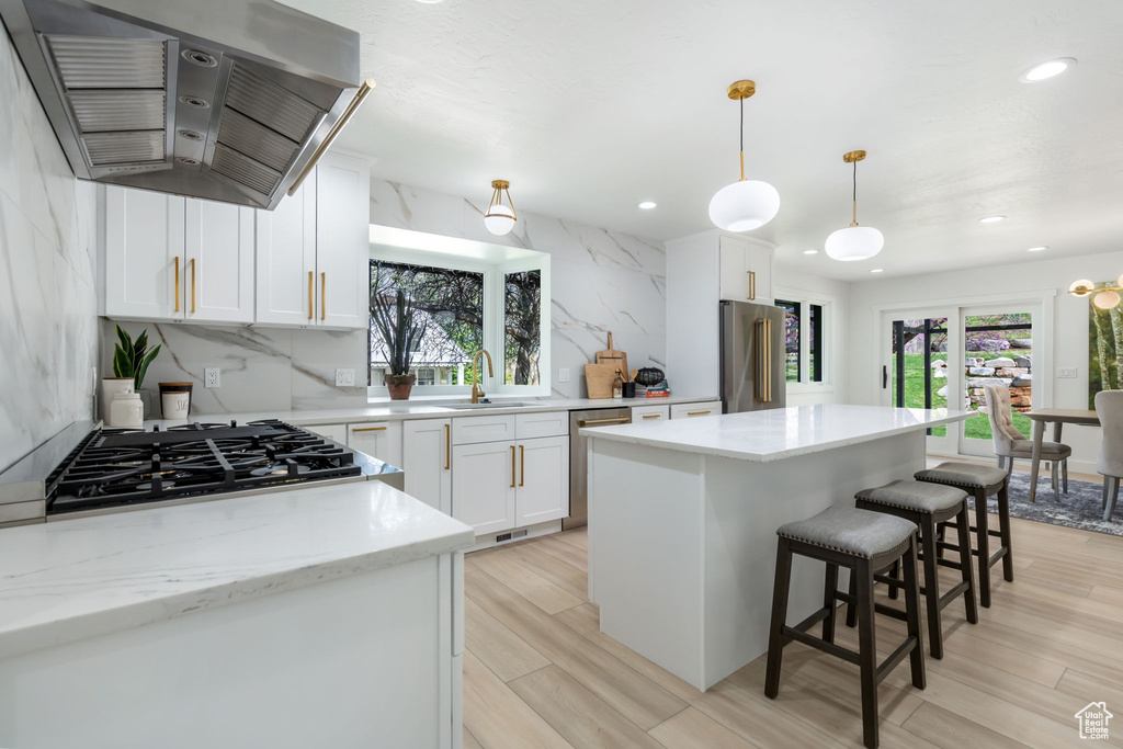 Kitchen with backsplash, appliances with stainless steel finishes, hanging light fixtures, wall chimney range hood, and a center island