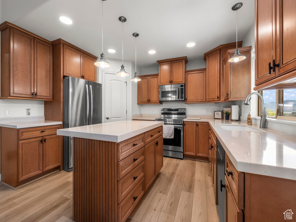 Kitchen with decorative light fixtures, appliances with stainless steel finishes, a center island, and light wood-type flooring