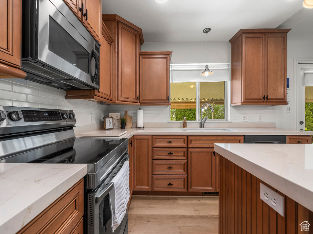 Kitchen with decorative light fixtures, backsplash, stainless steel appliances, sink, and light hardwood / wood-style floors