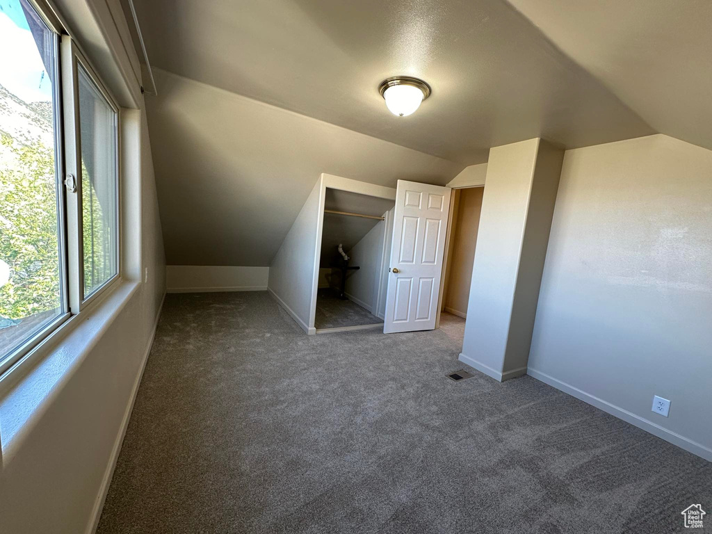 Unfurnished bedroom with vaulted ceiling, a closet, and dark colored carpet